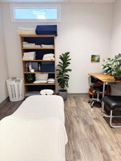 Massage bed in center of Massage Room 2 with clean sheets displayed on a shelf nearby