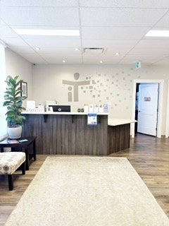 Reception area and desk with three different chairs for sitting, a variety of teas to choose from, and a water dispenser. Lots of natural light and various potted plants.
