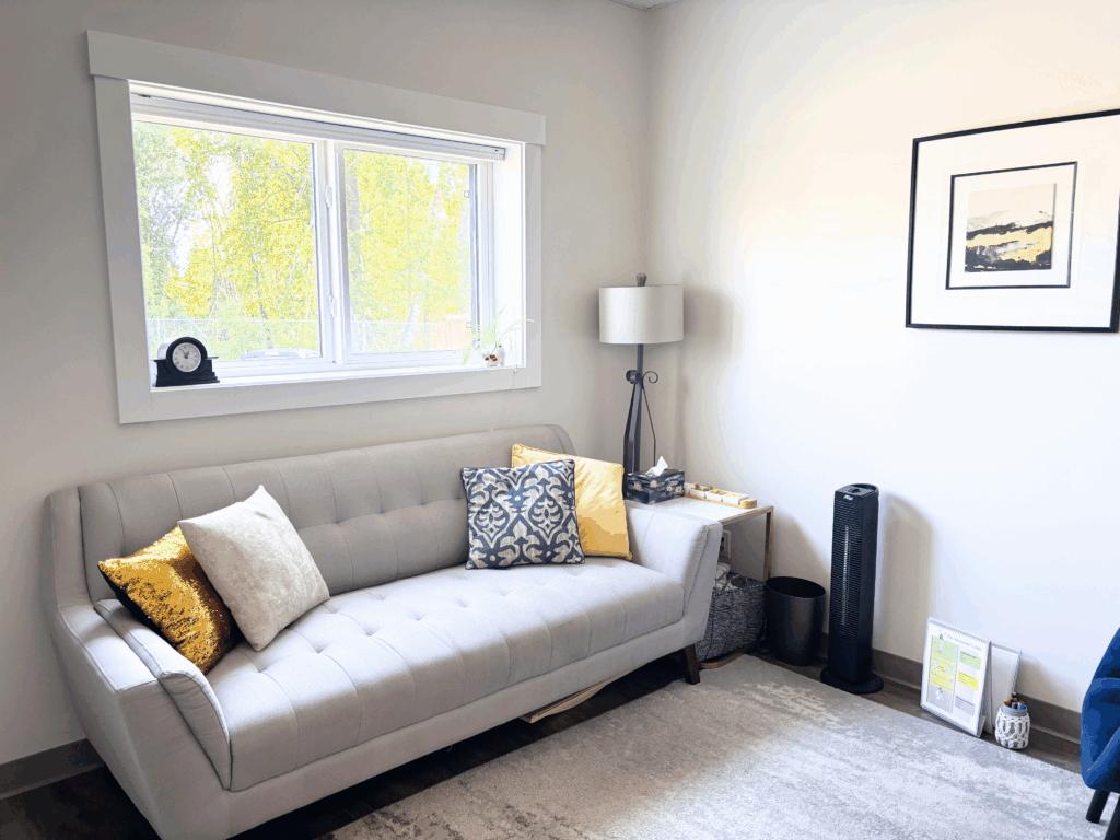 Clean office with a grey couch and a large window with natural lighting